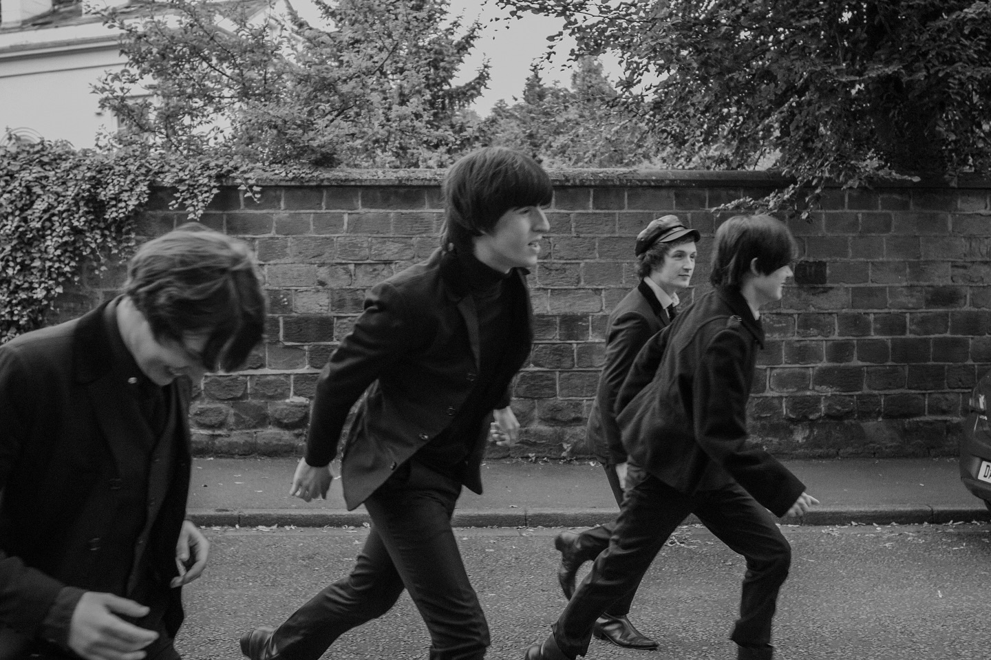 Four men dressed in black with long hair to look like The Beatles.